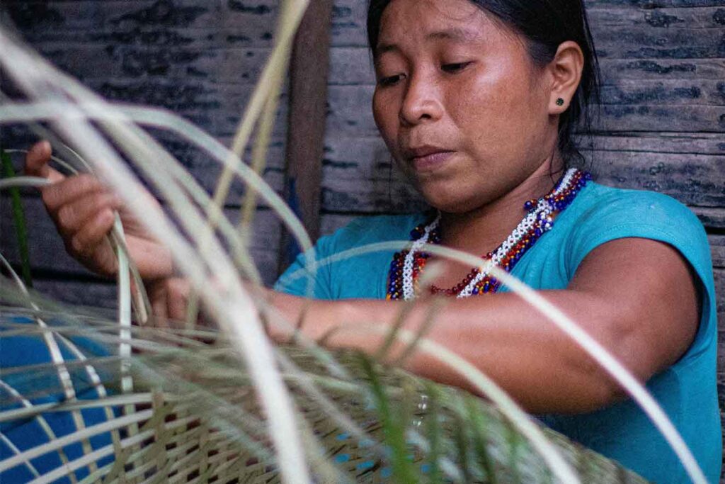 Mujer indígena del Chocó tejiendo con fibras naturales, artesanía tradicional del Pacífico colombiano.