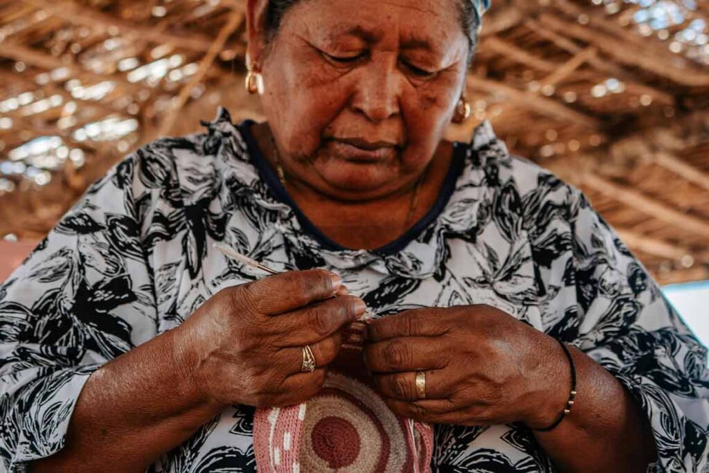Artesana Wayuu elaborando una mochila tradicional con hilos de colores, técnica ancestral del norte de Colombia.