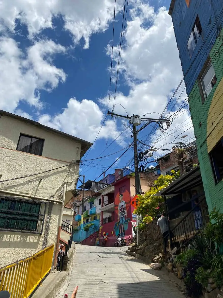 Calle en Constelaciones, Medellín, decorada con murales vibrantes en fachadas de viviendas comunitarias.