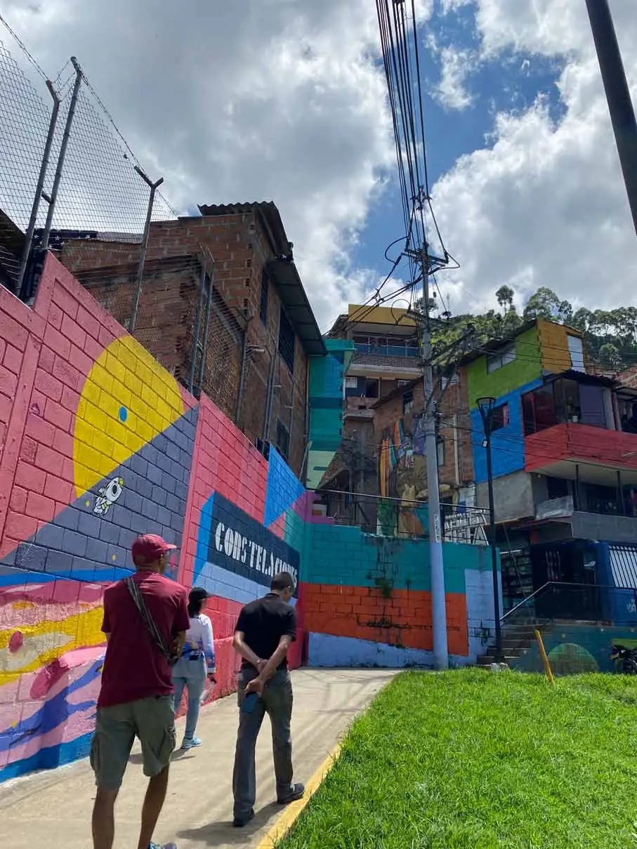 Viajeros recorren las calles de Constelaciones en Medellín, rodeados de arte urbano y experiencias de turismo comunitario.