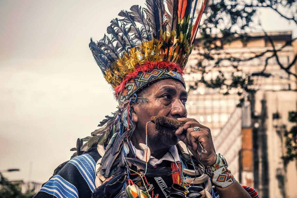Indígena del Putumayo con atuendo tradicional: ruana tejida y corona de plumas, símbolo de identidad cultural.