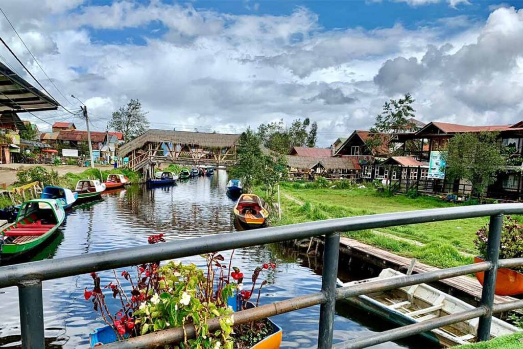 Barcas de colores flotando en la Laguna de La Cocha, Nariño, rodeadas de naturaleza andina y arquitectura lacustre.